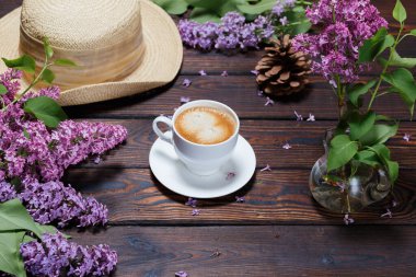 Şapka, çam kozalağı, beyaz kahve koyu ahşap arka planda duran bir demet leylak. Masada düşmüş leylak çiçekleri. Metin için boşluk. Seçici odaklanma. Sevgililer Günü ve Anneler Günü geçmişi.