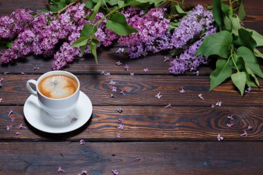 Beyaz bir fincan kahve bir demet leylak koyu ahşap arka planda yatar. Masada düşmüş leylak çiçekleri. Metin için boşluk. Seçici odaklanma. Sevgililer Günü ve Anneler Günü geçmişi.