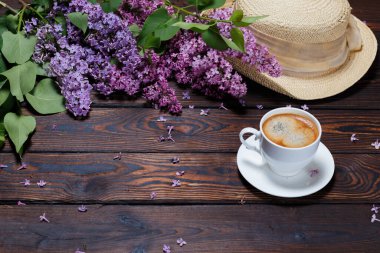Şapka, beyaz kahve bir demet leylak koyu ahşap arka planda yatıyor. Masada düşmüş leylak çiçekleri. Metin için boşluk. Seçici odaklanma. Sevgililer Günü ve Anneler Günü geçmişi.