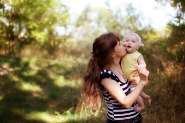 Annesi, kızını doğayla iç içe büyüttü. Bebek uçuyor. Annemin uzun saçları ve çizgili kıyafetleri var. Anneler Günü 'nün konsept fotoğrafı, ebeveynlik, babalık. Seçici odaklanma. Orta keskinlikte.