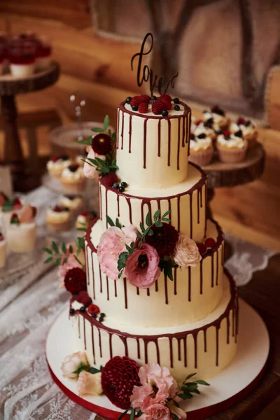 Cream wedding cake with flowers stands on a table with kendibar.