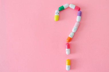 Renkli kapsüller pembe arkaplan üzerinde kopyalama alanı olan bir soru işareti şeklinde serili