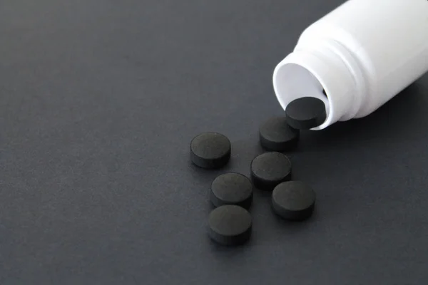 Una Bottiglia Bianca Pillole Nere Carbone Attivo Sfondo Nero Con — Foto Stock