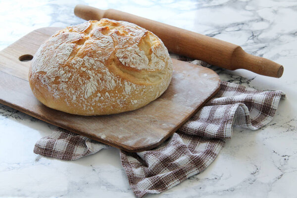Свежий домашний хрустящий круглый хлеб на деревянной доске и льняная клетчатая салфетка, вид сверху. Здоровый пресный хлеб. Французский хлеб. Хлеб на закваске
