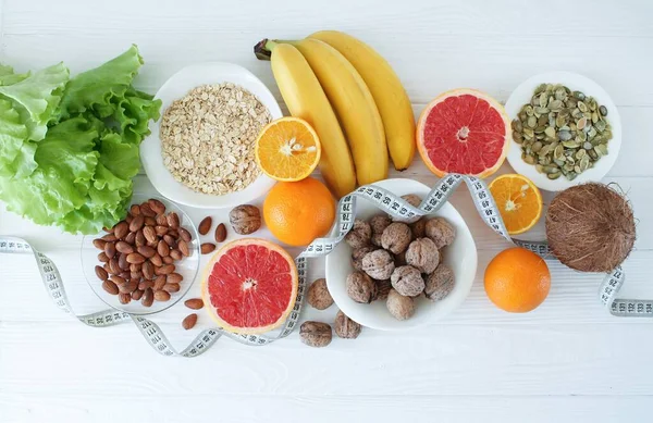 Fresh fruits and food with tape measure over white wooden background. Top view. Diet plan concept