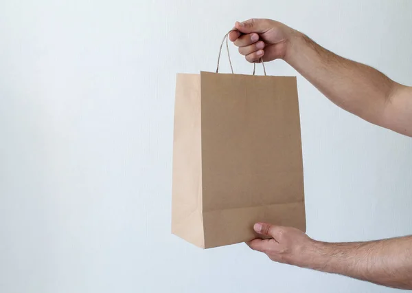 Yakından çekilmiş bir adam, beyaz arka planda izole edilmiş, içi boş, boş, geri dönüşümlü bir kağıt torbayı elinde tutuyor. Teslimat hizmeti konsepti. Paketleme şablonu maketi. Mesaj için yer var. Reklamcılık