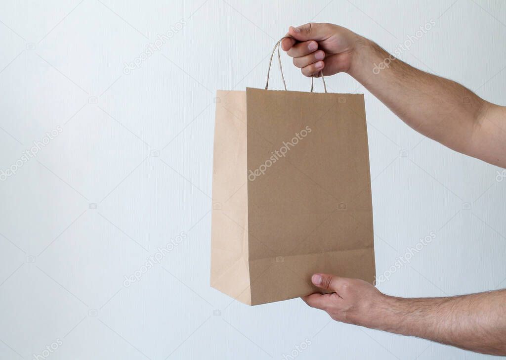 Close-up man holds in hand brown clear empty blank recycled craft paper bag for takeaway isolated on white background. Delivery service concept. Packaging template mock up. Space for text. Advertising