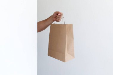 Yakın plan adamı açık gri arka planda paket almak için elinde açık kahverengi, boş, boş bir kağıt torba tutuyor. Paketleme ve teslimat hizmeti kavramı