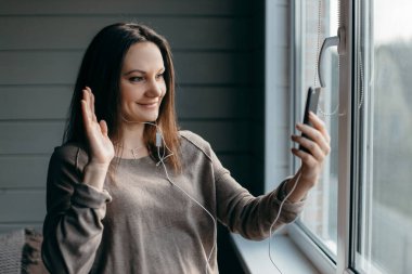Sağlıklı genç esmer kadının portresi evde akıllı telefonuyla görüntülü konuşma yapıyor, zoom toplantısını internet uygulaması, sosyal uzaklık, evden çalışma, uzaktan konsept çalışması