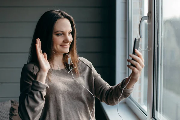 Sağlıklı genç esmer kadının portresi evde akıllı telefonuyla görüntülü konuşma yapıyor, zoom toplantısını internet uygulaması, sosyal uzaklık, evden çalışma, uzaktan konsept çalışması