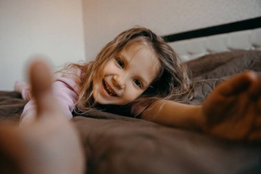 Covid-19 karantinası sırasında çocuk pijama partisinde iyi eğlenceler. Yatakta yatan ve gülümseyen komik küçük kız..  