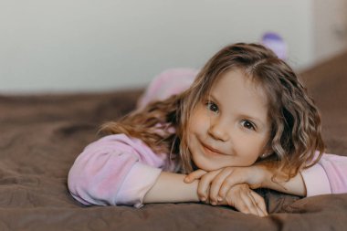Güzel kız Covid-19 karantinası sırasında evde pijama partisi veriyor. Yatakta yatan ve gülümseyen komik küçük kız. Hepimiz iyi olalım.!