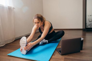 Oturma odasında egzersiz yapan genç bir kadın. Video dersi. Genç bir kadın çevrimiçi antrenman izlerken egzersizleri tekrarlıyor. Güzel genç bir kadın evde spor yapıyor.