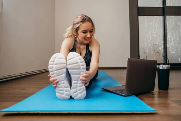 Oturma odasında egzersiz yapan genç bir kadın. Video dersi. Genç bir kadın çevrimiçi antrenman izlerken egzersizleri tekrarlıyor. Güzel genç bir kadın evde spor yapıyor.