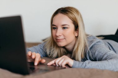 Kadın oturma odasında yatakta uzanıyor ve Zoom 'un akrabalarıyla bilgisayarla konferans görüşmesi yapıyor. Zoom Çağrı Toplantısı. Merkez ofis. Evde kal ve Coronavirus sırasında ev kavramından uzak dur.