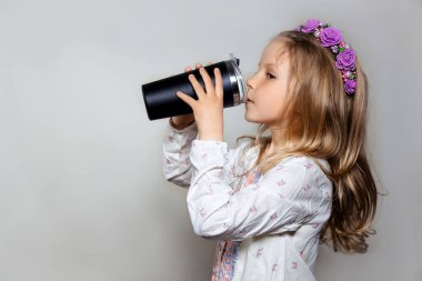 Siyah bardaktan su içen beyaz elbiseli güzel bir kız profili ve gri izole edilmiş arka planda mor bir çelenk. . 
