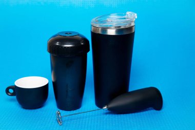 Siyah termo bardak, kahve fincanı ve mikser mavi arka planda izole edilmiş.