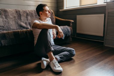 Ciddi bir genç adam elinde telefonla yerde oturuyor ve şöyle düşünüyor: 