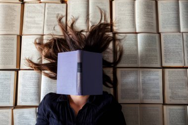 Sınav hazırlıklarından sonra menekşe kitapla kitapların arkasında yatan uzun saçlı öğrenci kız.