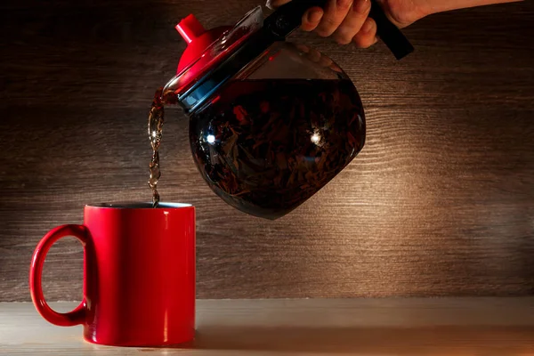 Tea being poured into red tea cup on wooden background