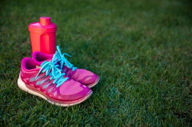 Mavi kordonlu pembe spor ayakkabılar ve taze yeşil çimen arka planında pembe su savaşı. Spor ayakkabı konsepti