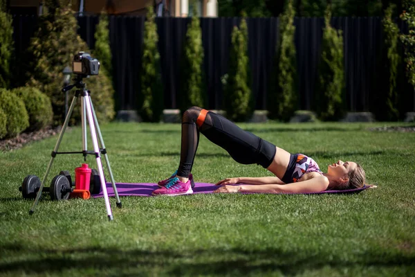 Sportive fitness coach woman recording video blog  by camera about  workout  training at the garden with fresh green grass near house.