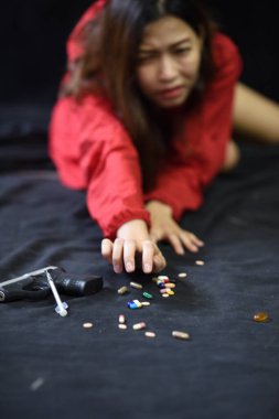 Genç Asyalı kadının karanlık odada yerde tek başına yatması bulanıklaşmıştı. Yerde bir sürü uyuşturucu ve silah var. umutsuz konsept (düşük tuş)