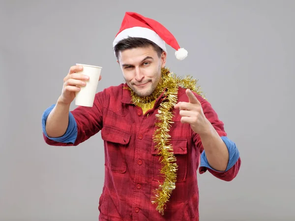 Śmieszne młody człowiek pijany kapeluszu Santa trzymając kubek papierowy — Zdjęcie stockowe
