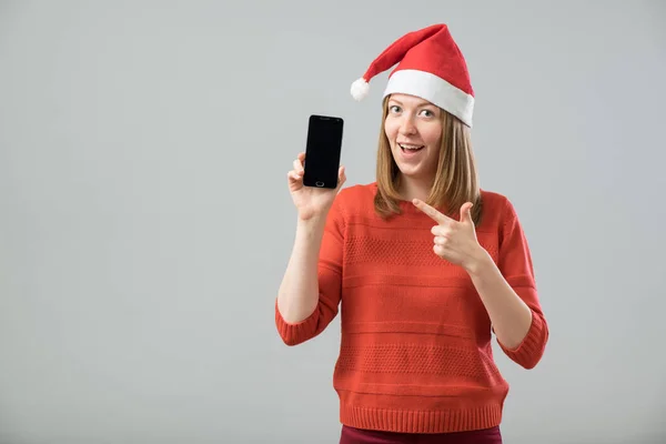 Νεαρή γυναίκα με καπέλο Santa δείχνει smartphone — Φωτογραφία Αρχείου