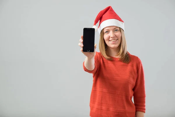 Молодая женщина в шляпе Санты показывает смартфон — стоковое фото