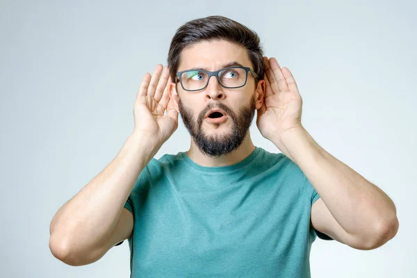 Fröhlicher junger Mann hält Hand in Ohr — Stockfoto