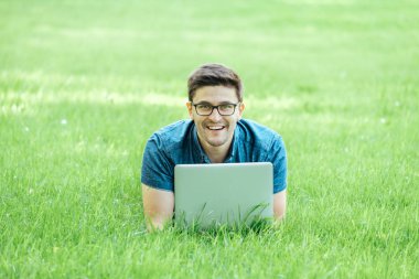 Çim üzerinde yalan ve dizüstü bilgisayar kullanarak genç adam