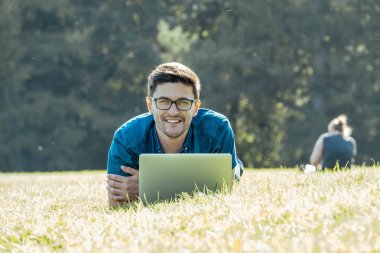Çim üzerinde yalan ve dizüstü bilgisayar kullanarak genç adam