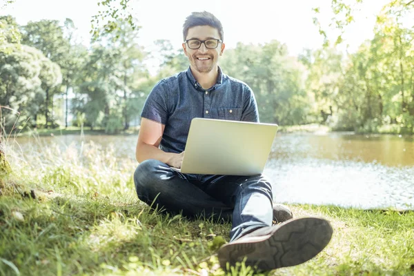 Dizüstü bilgisayar açık çimlere oturup ile genç adam
