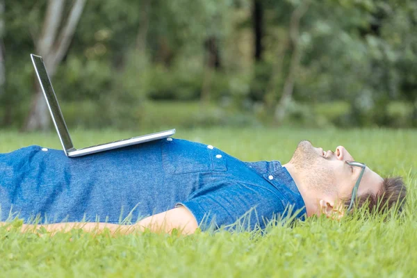 Tired freelancer lying in the park with laptop — Stock Photo, Image