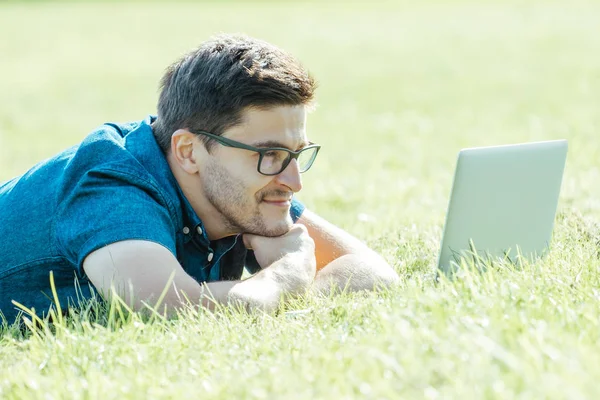 Çim üzerinde yalan ve dizüstü bilgisayar kullanarak genç adam