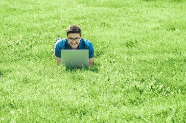 Çim üzerinde yalan ve dizüstü bilgisayar kullanarak genç adam