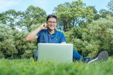 Çimenlerin üzerinde otururken Smartphone kullanan genç adam