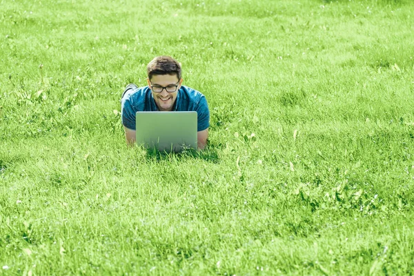 Jovem deitado na grama e usando laptop — Fotografia de Stock