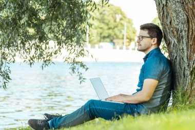 Adam açık havada doğa içinde oturan dizüstü bilgisayar ile