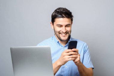 Cep telefonu kullanarak ve dizüstü bilgisayar ile masadan neşeli adam