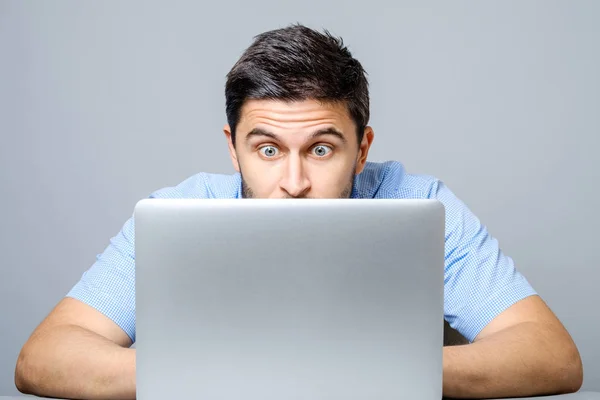 Joven hombre sorprendido en camisa azul usando el ordenador portátil — Foto de Stock