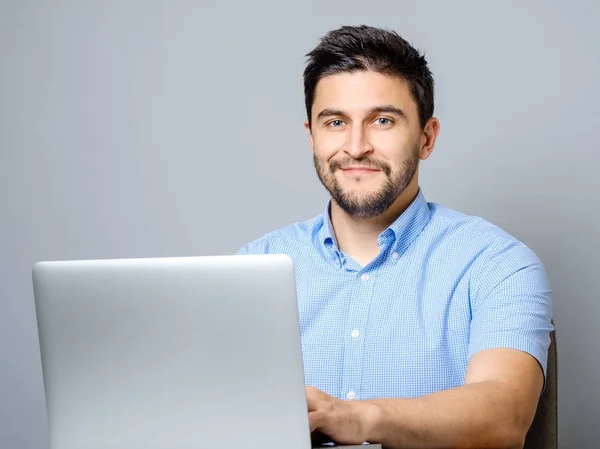 Retrato del joven sonriente sentado en el escritorio con el ordenador portátil — Foto de Stock