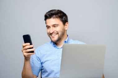 Cep telefonu kullanarak ve dizüstü bilgisayar ile masadan neşeli adam