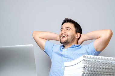 Laptop ile masada oturan ve germe neşeli bir genç adam. Gri izole