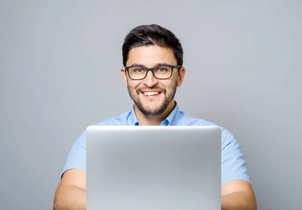 Портрет молодого усміхненого чоловіка, що сидить за столом з ноутбуком — стокове фото