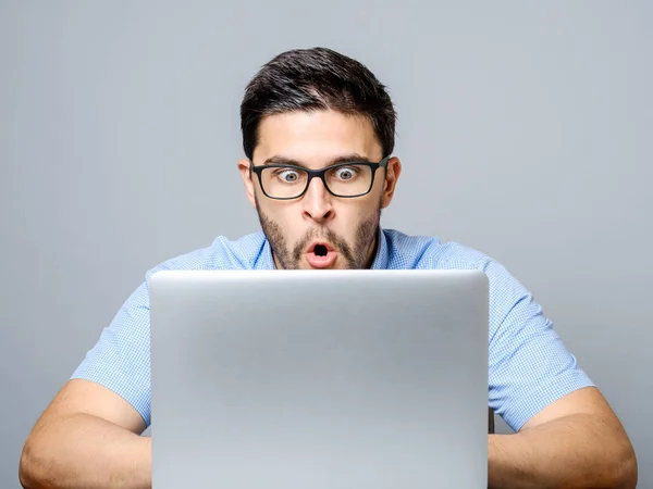 Junger schockierter Mann in blauem Hemd benutzt Laptop — Stockfoto