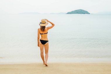 Kumsalda duran güneş şapkalı ve bikinili güzel bir kadın.