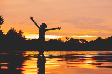 Gün batımında kadın silueti. Suyun yansımasıyla gökyüzü.