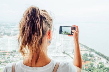 Genç kız büyük şehrin fotoğrafını çekmek için cep telefonu kullanıyor.